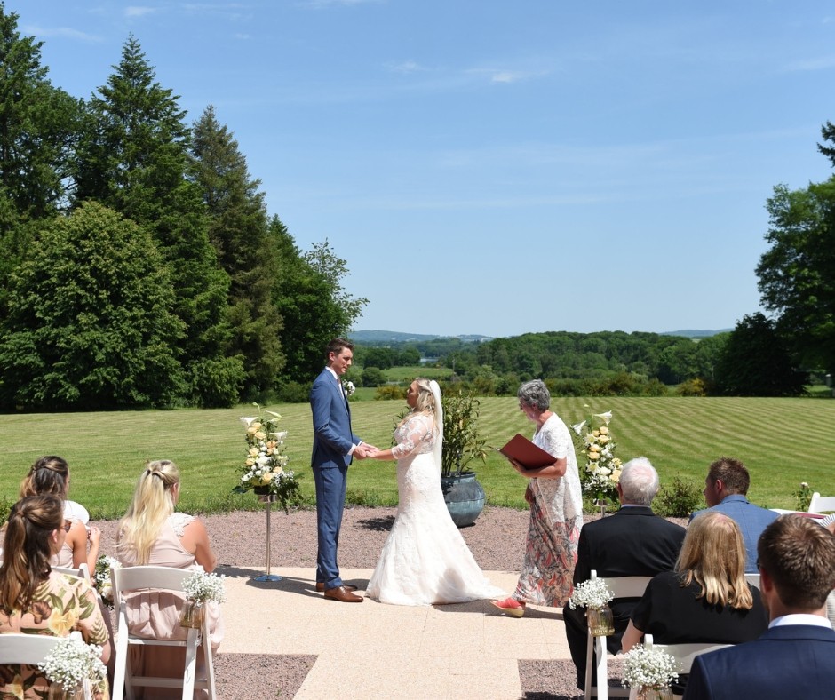 Couple saying their wedding vows during their outdoor ceremony at Chateau de la Cazine with blue skies and lush French countryside as their backdrop 