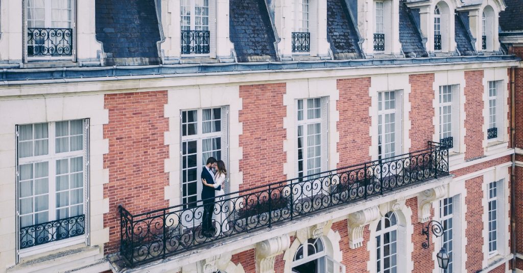 Emilie and Vael wedding day kissing on the balcony of the chateau de la cazine french chateau redbrick neo baroque wedding venue