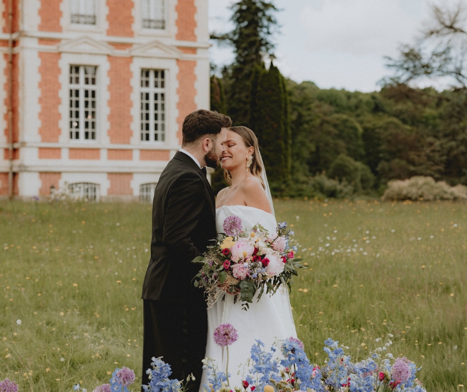 Bride and Groom Kiss in front of the intimate chateau wedding venue Chateau de la Cazine. The bride holds her colourful bouquet.